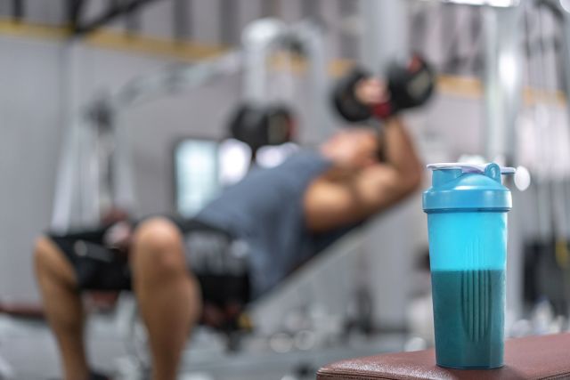 a man lifts weights in the background with a container of a protein supplement in the foreground