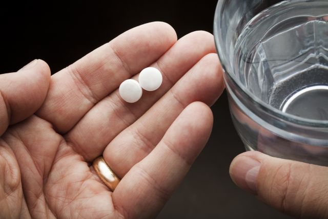 Man holding aspirin pills and a glass of water