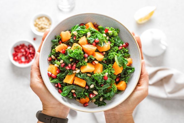 A fresh bowl of kale salad accented with fresh mango and pomegranate seeds