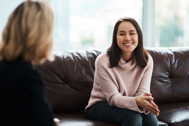 a young women smiles as she sits on a coach for a psychotherapy session