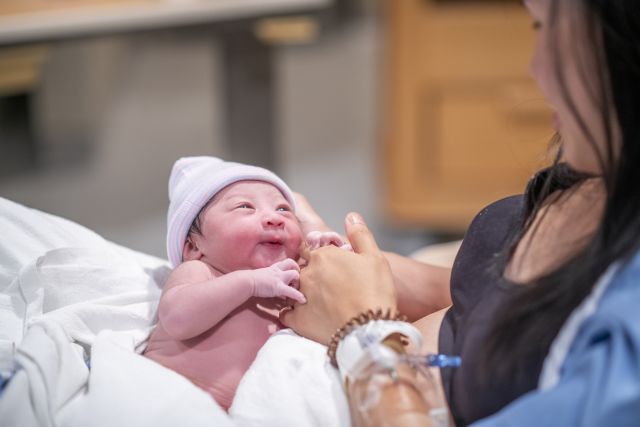 a happy Asian parent in a hospital cradles their newborn baby