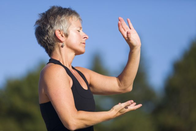 a middle aged woman does tai chi in a sunny wooded area