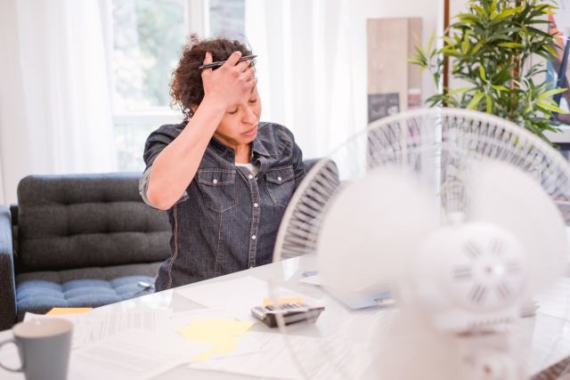 A woman feels her forehead in front of a fan.
