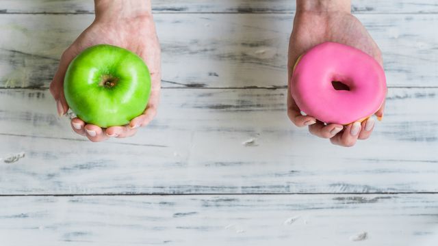 One hand holds an apple, one hand holds a doughnut. 