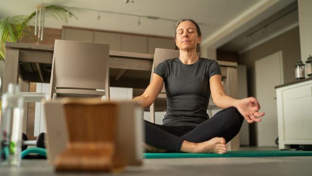 Older woman meditates in her living room. 
