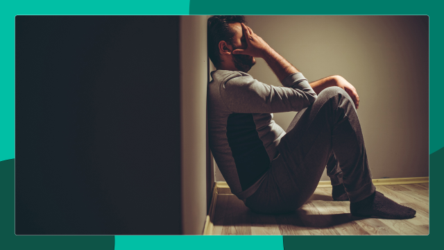 A man sits alone in a dark room. Many people with HIV struggle with the mental burden of living with a chronic illness.