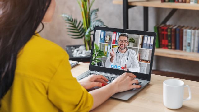 A woman connects with her dermatologist using a telehealth application on her computer.