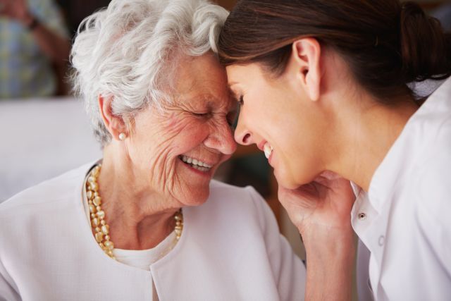 Smiling adult woman and senior grandmother with Alzheimer’s touching foreheads