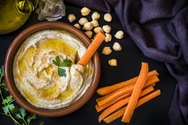A bowl of hummus, which is good for cholesterol, is ready for snacking with a side dish of carrot sticks.