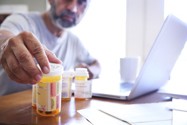 A man with bipolar disorder reaches for one of his prescription medication bottles as he sits at his dining room table. 
