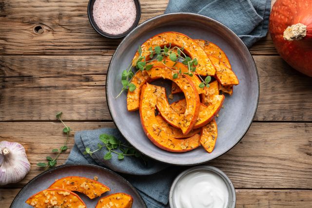 a roasted, sliced pumpkin, pictured on a plate, garnished with fresh green herbs