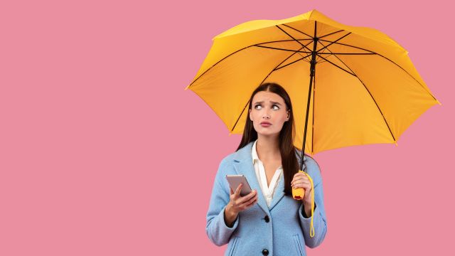 A young woman with an umbrella checks the weather app on her phone.