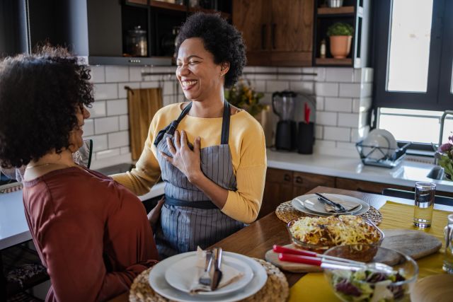 two middle aged Black people share a laugh while they cook healthy food in a home kitchen