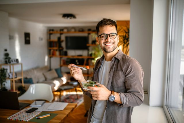 young man with glasses eating salad indoors