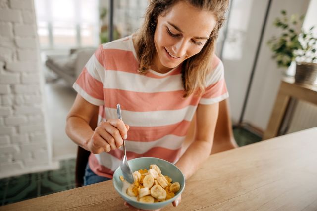 view of woman enjoying a healthy breakfast of cold cereal with bananas on top