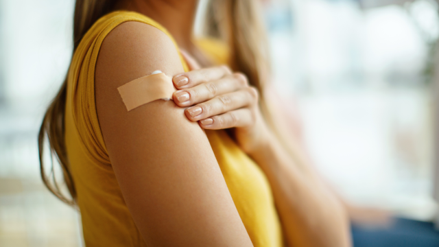 Closeup of a young woman's upper arm with a cotton ball covered by a bandaid following an HPV vaccination
