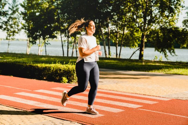 Young woman in athletic clothing wearing headphones jogging through the park for interval training