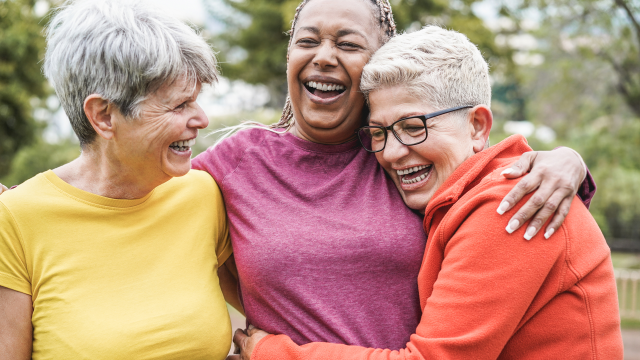 Group of three woman outdoors hugging and laughing, enjoying community and fitness together