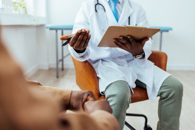 view of an unidentifiable man sitting in an exam room listening to a doctor explain the results of his medical tests