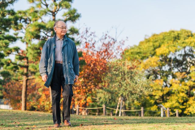 an older Asian man walks in the park on an autumn day