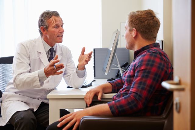 Young man sitting with a male doctor discussing health in an exam room