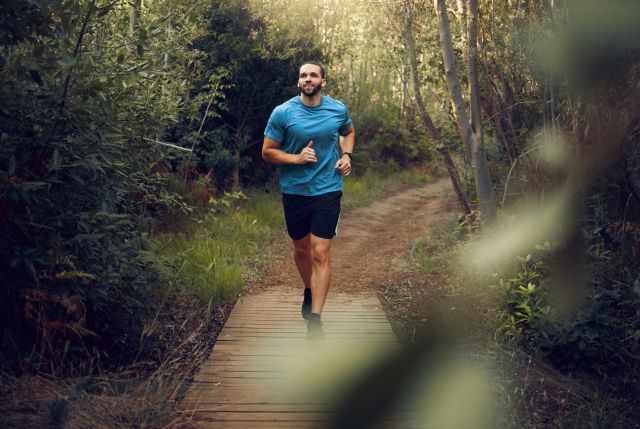 Young man running on a path through a thick forest area, proactive exercise to promote good heart health
