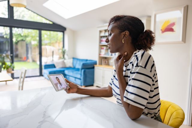 a middle aged Black woman with a sore throat conducts a telemedicine appointment with her healthcare provider