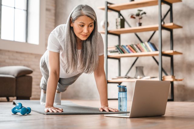 a middle aged Asian American woman does a plank yoga pose at home to strengthen her bones