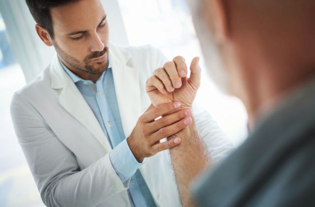 young male doctor testing wrist of older male patient