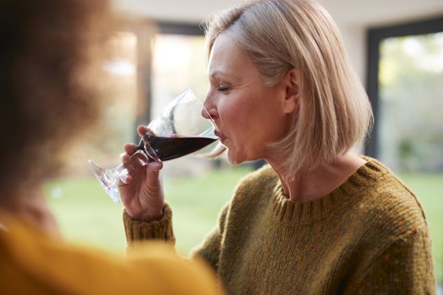 a middle aged white woman drinks a glass of red wine