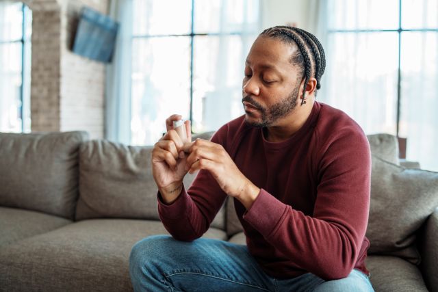 a Black man sits on a couch preparing to take his inhaled asthma medication
