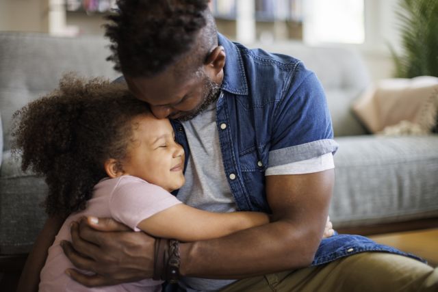 adult Black male hugging a young child, presumably his daughter