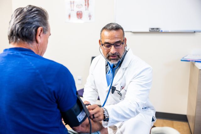 a bearded Latino middle aged doctor checks an older adult patient's blood pressure as part of a regular checkup
