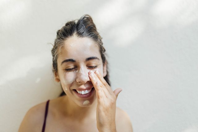 A young woman applies sunscreen to her face. Wearing sunscreen helps protect the skin from sun damage that could make atopic dermatitis symptoms worse.