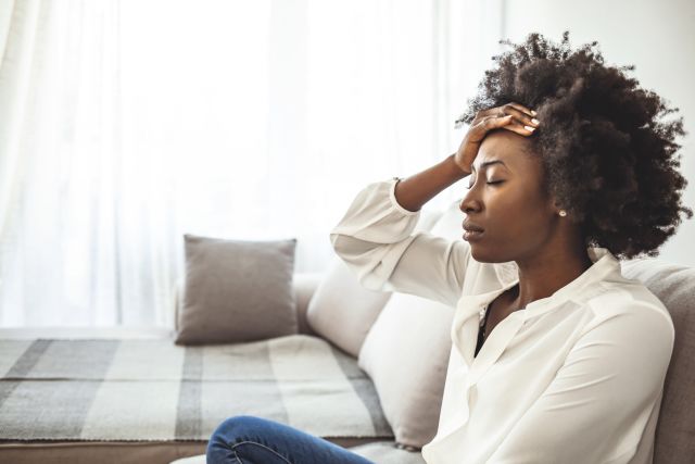 a young Black woman who is stressed out places her hands on her head 