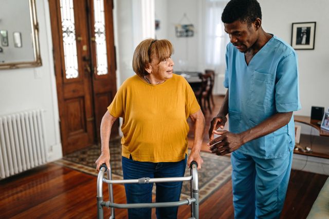 young male occupational therapist helps older adult woman use walker