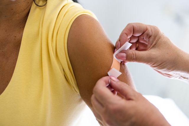 a closeup shot of a woman's arm with a bandage, after having received a COVID vaccine shot