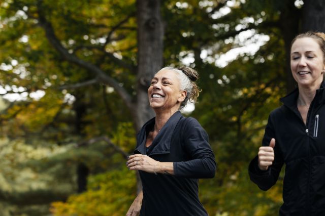 middle aged adult white woman jogs in park with friend, smiling and enjoying the activity