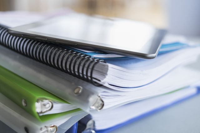 stack of notebooks and binders with digital phone or tablet on top