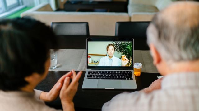 A senior couple consults with a healthcare provider over a video call on a laptop.
