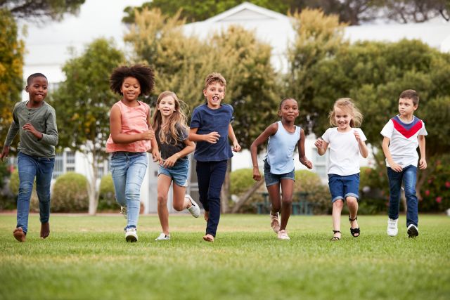 A group of children of different races and ethnicities run across a grassy yard.