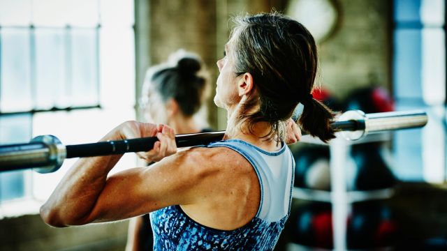 A senior woman lifts weights in a gym.