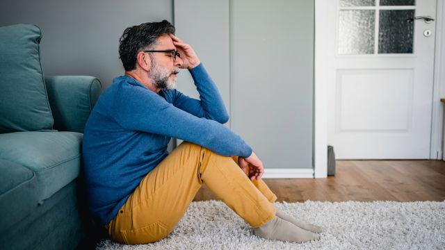 A middle-aged man sits on the floor of his living room, struggling with low mood and depression.