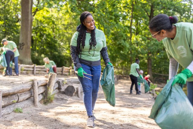 A young Black woman smiles as she volunteers to help clean up a local park to help improve the environment and ease feelings of eco-anxiety.