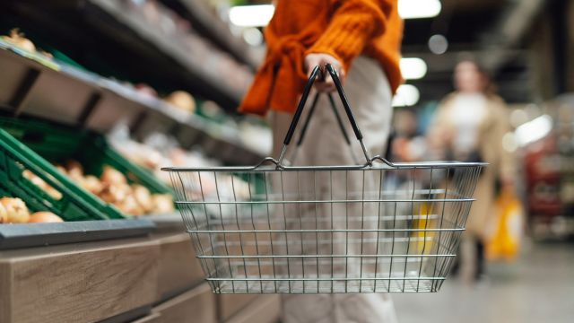 A woman with a grocery basket shops for produce in a supermarket.