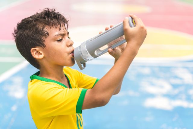 A young boy takes a drink of water from a water bottle after playing sports on a hot day.