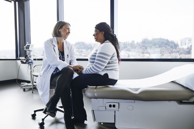 a young Black woman sits in an airy, light-filled doctor's office talking to a white woman doctor about a diagnosis of PCOS