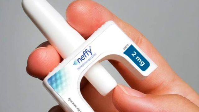 close up of a hand holding a bottle of neffy, a epinephrine nasal spray device