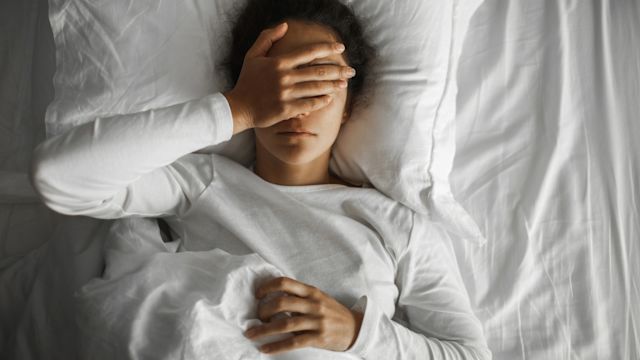 A woman covers her eyes with her hand as she wakes with a headache after a poor night's sleep.