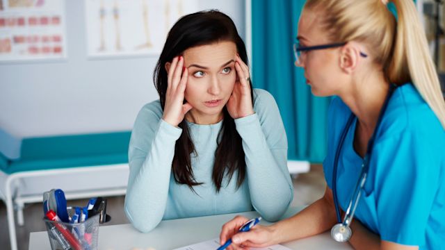 A visibly stressed woman describes her concerns to a healthcare provider during an appointment to discuss hereditary angioedema. High stress levels are a potential trigger for HAE episodes and may need to be addressed with prophylactic therapy.